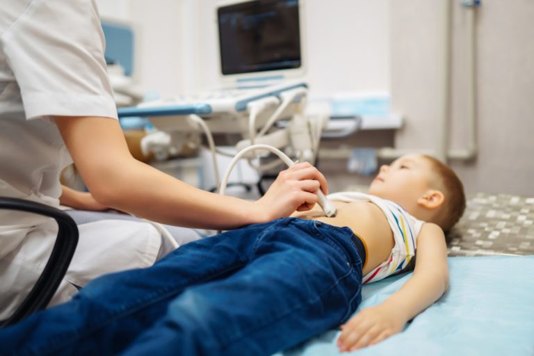 Boy undergoing thyroid ultrasound examination. Doctor examining kid throat in clinic with equipment.