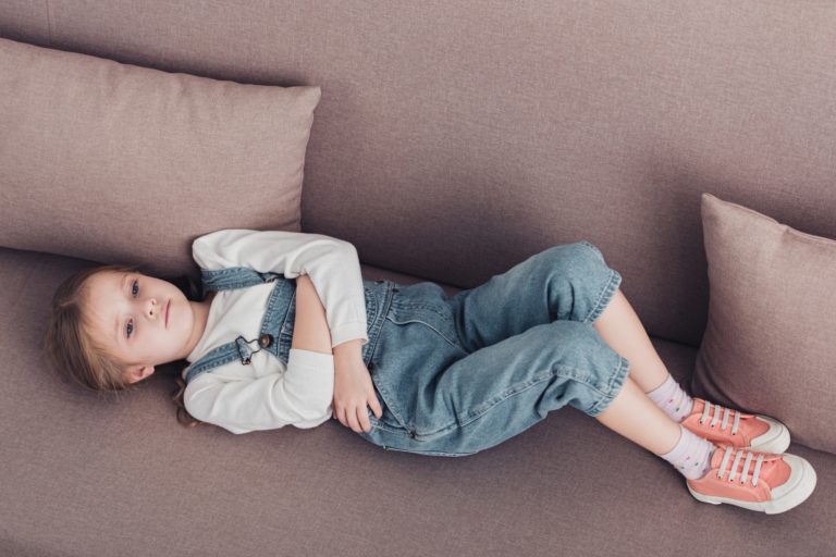 high angle view of sick child with stomach pain lying on sofa in living room